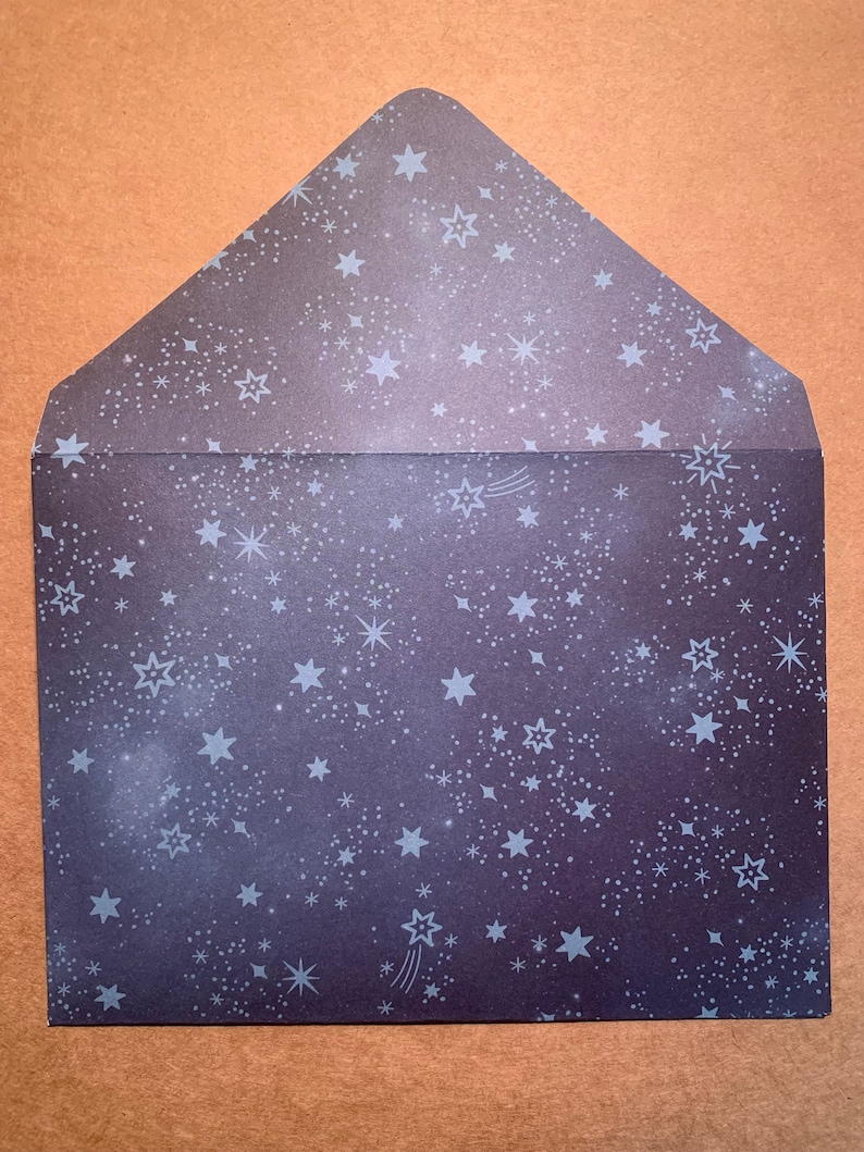 May include: A dark gray envelope with a white starry night pattern. The envelope is decorated with white stars and shooting stars.