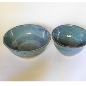 May include: Two ceramic bowls in a blue and brown glaze. The larger bowl is in the foreground and the smaller bowl is in the background.