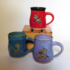 Peut inclure: Trois tasses en céramique avec des motifs de libellules. Les tasses sont en rouge, bleu et violet.