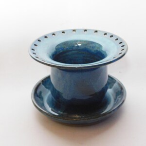 Pu&ograve; includere: Un vaso di fiori in ceramica blu con un sottovaso. Il vaso ha una parte superiore larga e piatta con fori attorno al bordo. Il sottovaso &egrave; dello stesso colore blu.