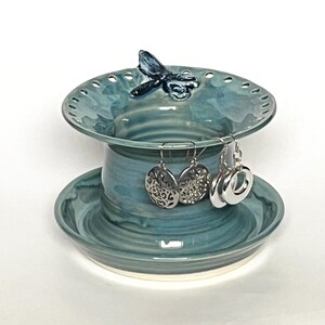 Pu&ograve; includere: Un porta gioielli in ceramica con una smaltatura blu e verde. Il porta gioielli ha una piccola libellula in cima e un piatto inferiore per anelli o orecchini.