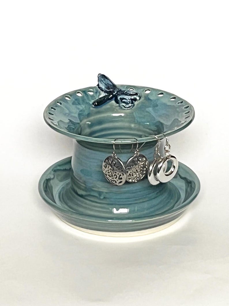 Pu&ograve; includere: Un porta gioielli in ceramica con una smaltatura blu e verde. Il porta gioielli ha una piccola libellula in cima e un piatto inferiore per anelli o orecchini.