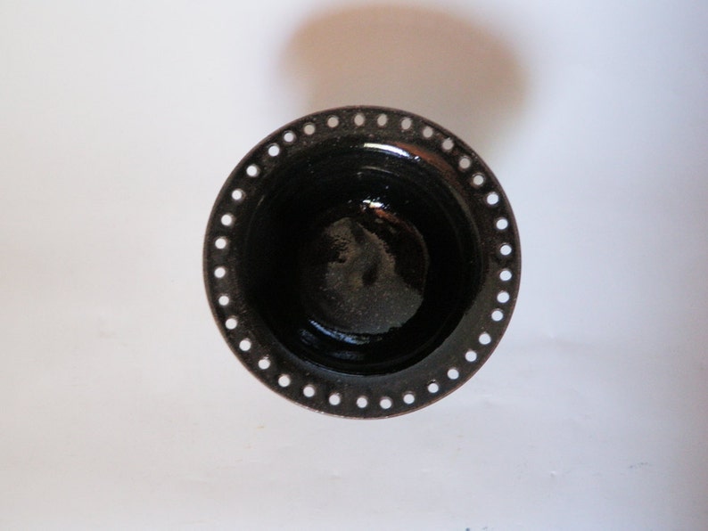 Puede incluir: Un peque&ntilde;o cuenco de cer&aacute;mica negro con un borde decorativo de peque&ntilde;os agujeros. El cuenco est&aacute; esmaltado y tiene un acabado brillante.