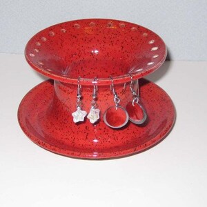 Pu&ograve; includere: Porta orecchini in ceramica rossa con design a due livelli. Il livello superiore ha fori per gli orecchini e il livello inferiore &egrave; un piattino. Ci sono tre paia di orecchini sul supporto.