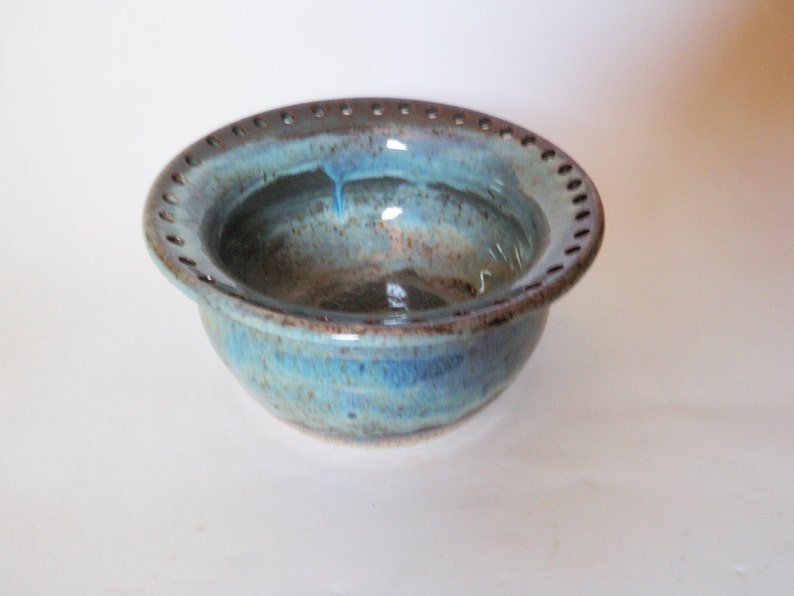 Puede incluir: Un cuenco de cer&aacute;mica azul y marr&oacute;n con un borde decorativo de agujeros. El cuenco tiene un esmalte moteado y un interior azul claro.