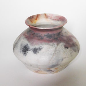 May include: A white ceramic vase with a rounded body and a wide mouth. The vase has a mottled glaze with shades of grey, black, and pink.