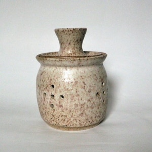 May include: A white ceramic jar with brown speckles and holes. The jar has a lid with a small opening in the center.