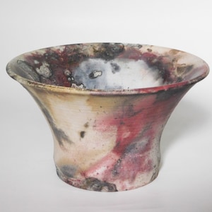 May include: A ceramic bowl with a wide, flared opening and a rounded base. The bowl is decorated with a mottled glaze in shades of white, grey, brown, and red.