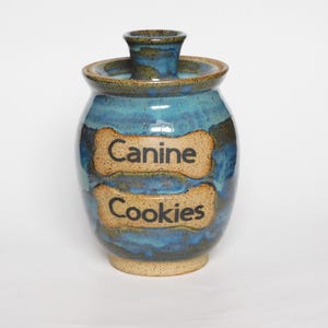 May include: A blue and brown ceramic jar with a lid. The jar has two bone-shaped labels that say "Canine Cookies".