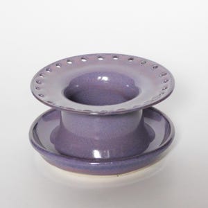 Pu&ograve; includere: Un infusore per t&egrave; in ceramica viola con una parte superiore larga e perforata e una base a piattino.