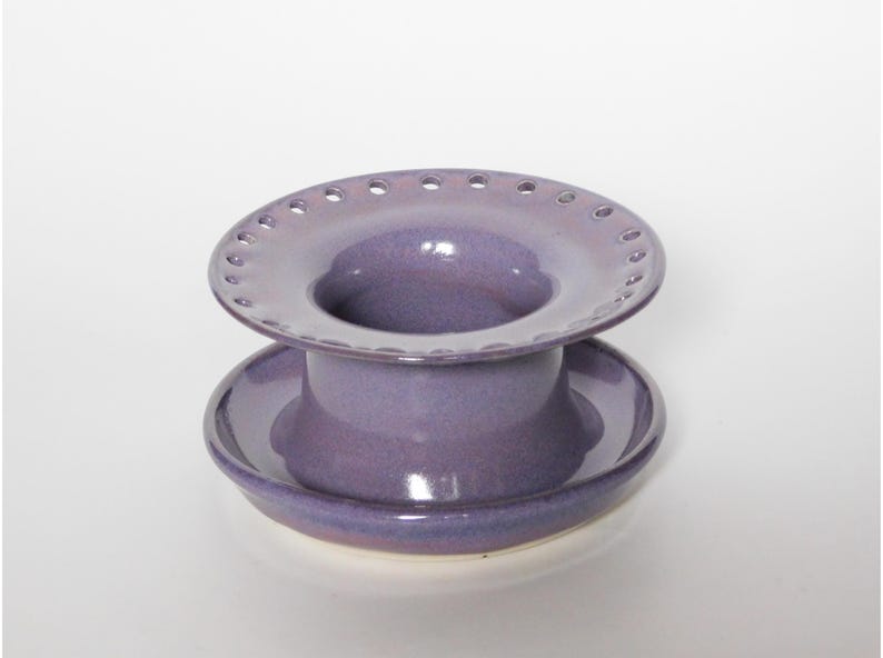 Pu&ograve; includere: Un infusore per t&egrave; in ceramica viola con una parte superiore larga e perforata e una base a piattino.