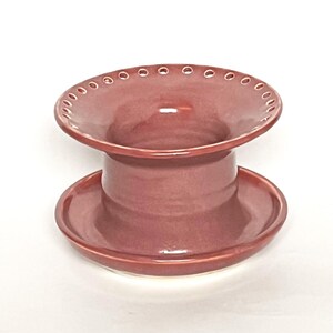 Pu&ograve; includere: Un vaso da fiori in ceramica color malva con una parte superiore larga e piatta e una base rotonda pi&ugrave; piccola. La parte superiore ha una fila di piccoli fori attorno al bordo.