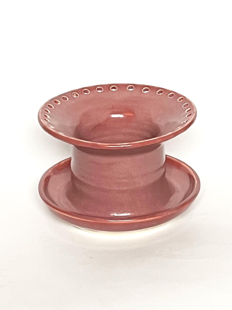 Pu&ograve; includere: Un vaso da fiori in ceramica color malva con una parte superiore larga e piatta e una base rotonda pi&ugrave; piccola. La parte superiore ha una fila di piccoli fori attorno al bordo.