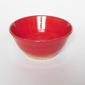 May include: A red ceramic bowl with a speckled glaze. The bowl has a slightly rounded bottom and a wide rim.