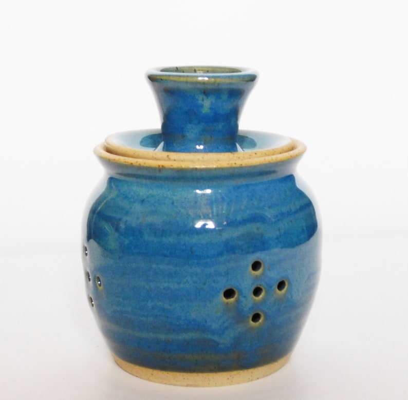 May include: A blue ceramic garlic keeper with a lid and holes for ventilation. The keeper has a light blue glaze with a subtle yellow hue.