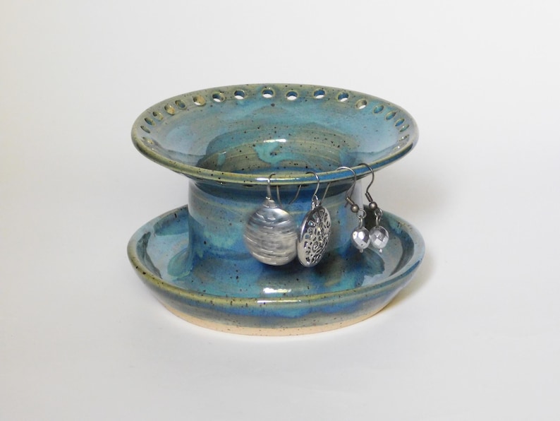 Pu&ograve; includere: Un porta orecchini in ceramica blu e verde con un design a pi&ugrave; livelli. Il livello superiore ha una ciotola larga e poco profonda con fori attorno al bordo. Il livello inferiore &egrave; una ciotola pi&ugrave; piccola e profonda. Tre orecchini d'argento sono appesi al livello superiore.