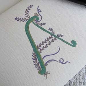 May include: A green and purple floral letter A with a decorative flourish. The letter is drawn in a whimsical style with a stylized lavender flower design.
