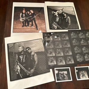May include: A set of eight black and white photographs of a punk rock band. The band members are wearing leather jackets, jeans, and bandanas. They are holding guitars and posing in front of a chain-link fence.