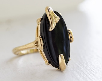May include: A gold ring with a black oval gemstone. The ring has a floral design on the band.