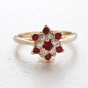 May include: A gold ring with a red and white flower design. The flower is made of small red and white rhinestones.