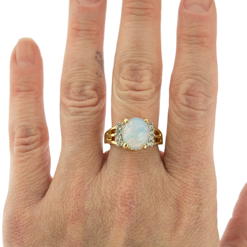 May include: A gold ring with a large oval opal gemstone surrounded by smaller clear gemstones.