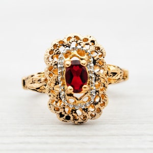 May include: A gold ring with a red gemstone set in a filigree design.