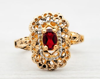 May include: A gold ring with a red gemstone set in a filigree design.