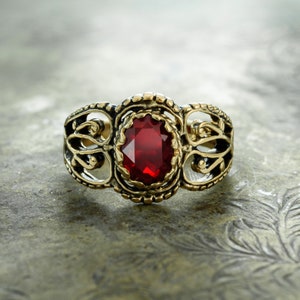 May include: A gold ring with an ornate design and a large, oval-shaped red gemstone.