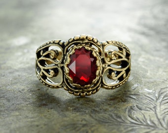 May include: A gold ring with an ornate design and a large, oval-shaped red gemstone.