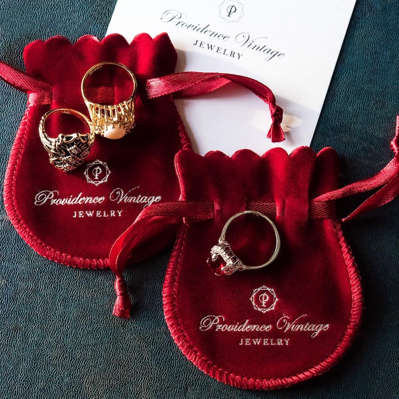 May include: Two red velvet jewelry pouches with gold and silver rings inside. The pouches have the text "Providence Vintage Jewelry" printed on them.