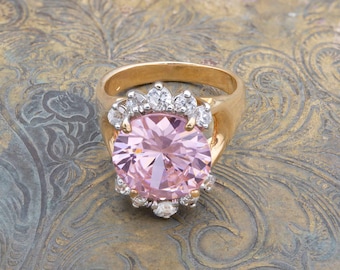 May include: A gold ring with a large pink gemstone surrounded by smaller clear gemstones.