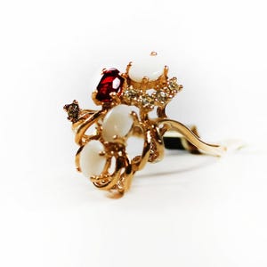 May include: A gold ring with a cluster of white and red gemstones. The ring has a delicate, intricate design.