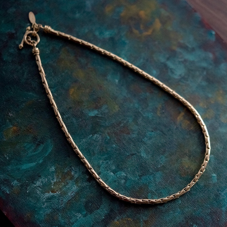 May include: A gold chain necklace with a box clasp. The chain is made of small, interlocking links.
