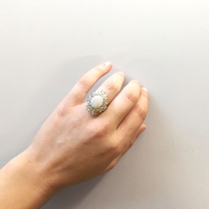 May include: A silver ring with a large oval-shaped white gemstone surrounded by smaller white gemstones.