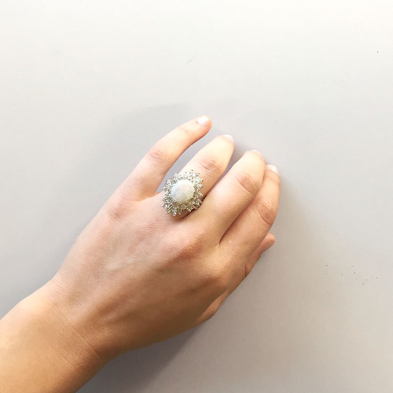 May include: A silver ring with a large oval-shaped white gemstone surrounded by smaller white gemstones.