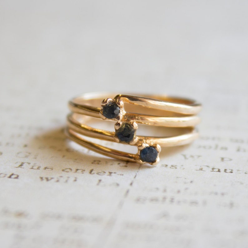 May include: A gold ring with three small black gemstones set in a row. The ring is made of three thin bands that are intertwined.