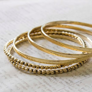 May include: A set of four gold-toned bangles, one with a beaded design. The bangles are stacked on top of each other.