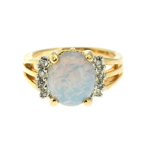 May include: A gold ring with a large oval-shaped opal gemstone and smaller clear gemstones around the setting.