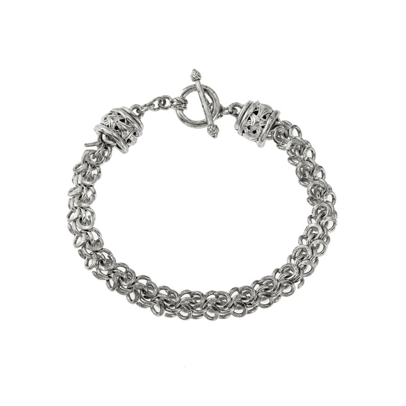 Puede incluir: Una pulsera plateada con cierre de palanca. La pulsera est&aacute; hecha de peque&ntilde;os anillos interconectados, creando un efecto de cota de malla. Cuentas cil&iacute;ndricas decorativas con intrincados patrones calados se encuentran en cada extremo de la pulsera.