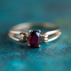 May include: A gold ring featuring a deep red oval gemstone set in a delicate, twisted band.