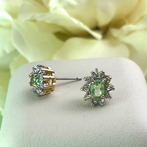 May include: A pair of gold and silver earrings with a green gemstone surrounded by smaller clear gemstones.
