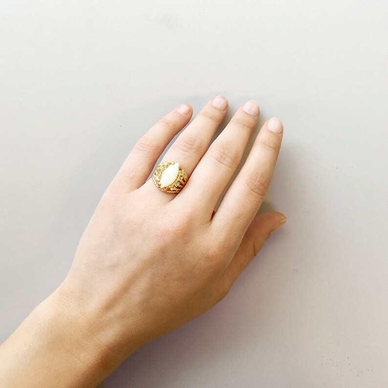 May include: A gold ring with a large white oval-shaped stone set in a detailed, ornate design.