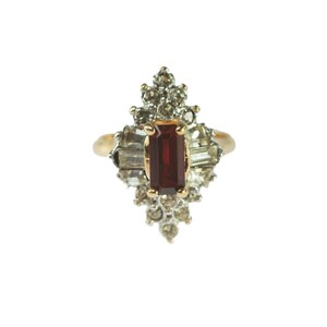 May include: A gold ring with a red rectangular gemstone surrounded by clear rhinestones.