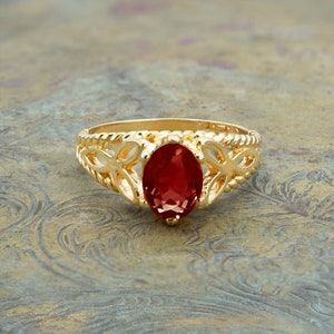 May include: A gold ring with a red oval gemstone set in a delicate filigree design.