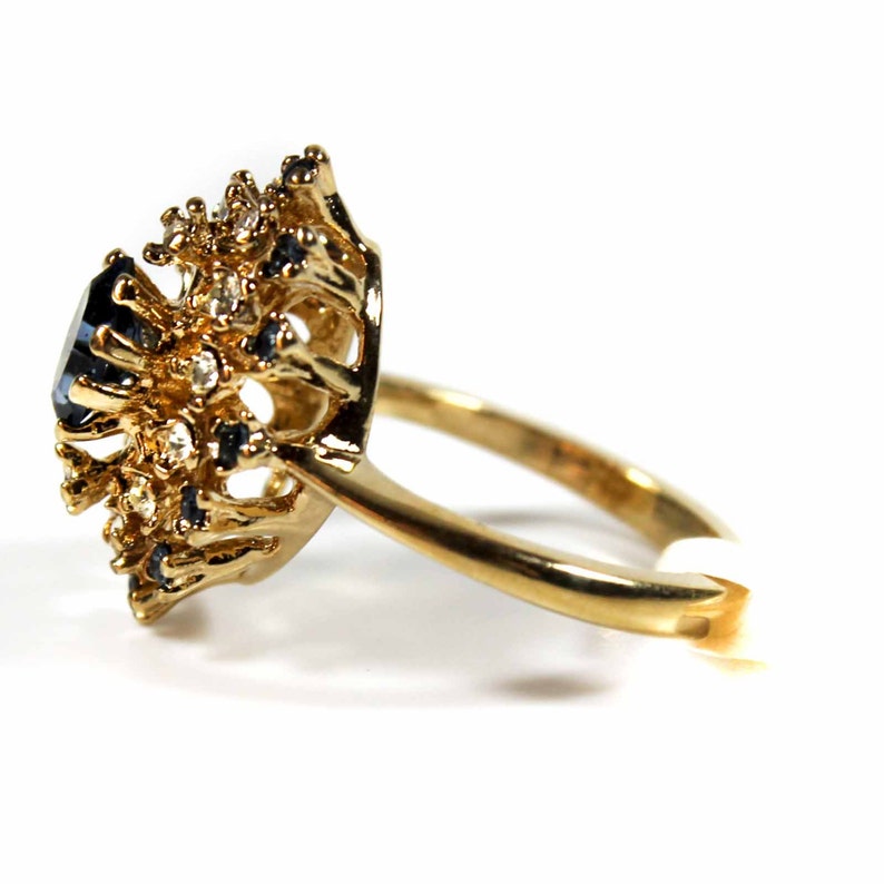 May include: A gold ring with a large blue gemstone surrounded by smaller clear and blue gemstones.