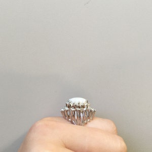 May include: A silver ring with a large white oval stone surrounded by smaller white stones.