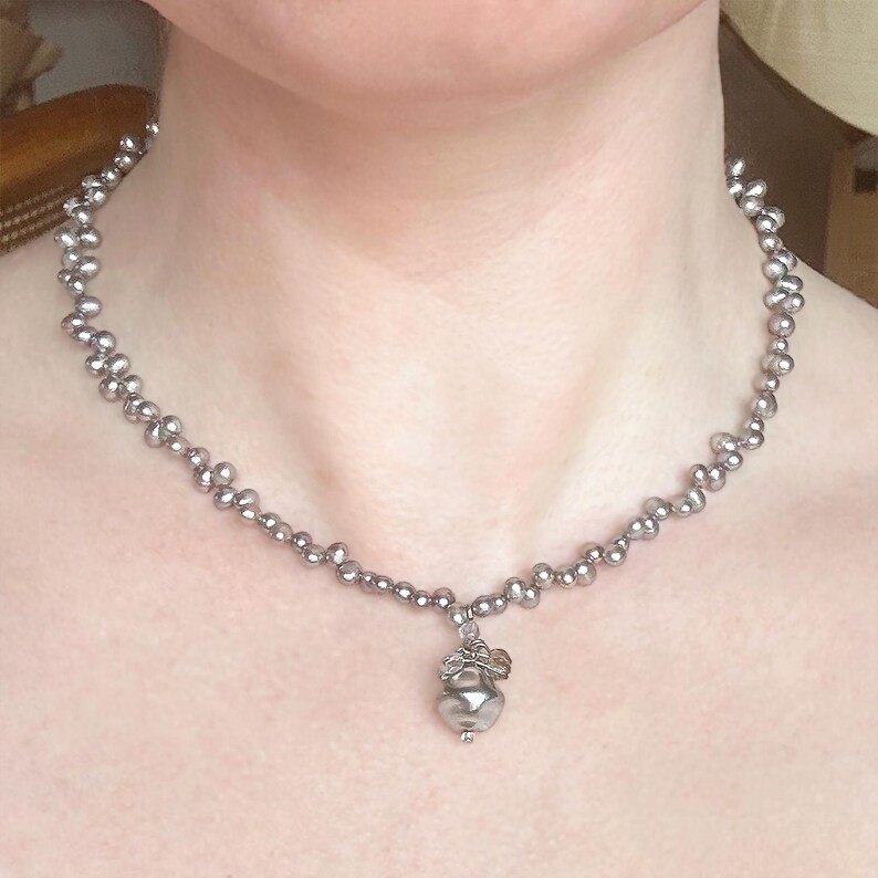 May include: A silver-toned necklace featuring a delicate chain of small, round beads. The necklace has a pendant with a decorative design. The jewelry is worn around the neck.
