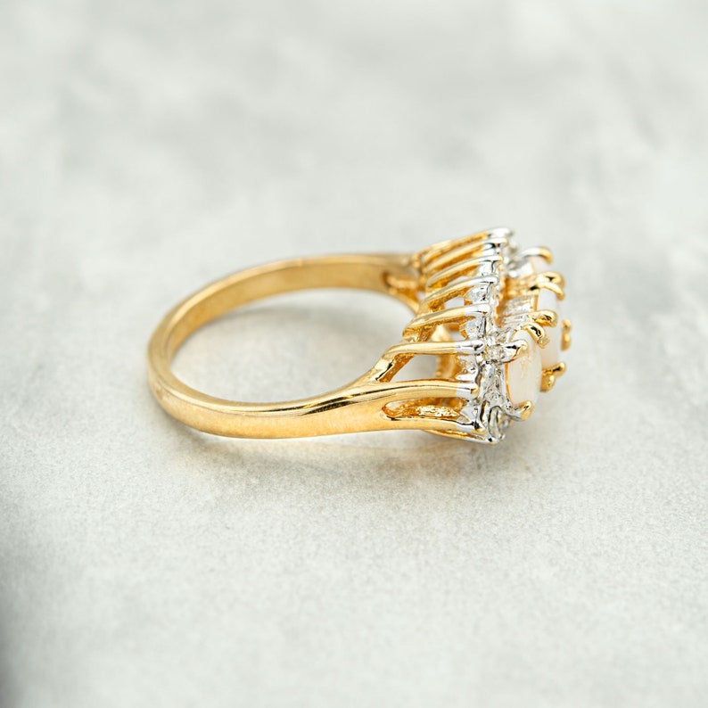 May include: A gold ring with a large oval opal stone surrounded by smaller diamonds. The ring is set in a delicate, intricate design.
