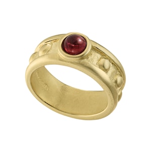 May include: A gold ring with a red gemstone set in a bezel setting. The band is textured and has small round accents.