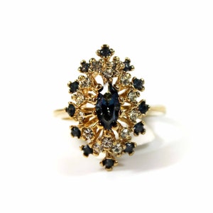 May include: A gold ring with a large blue gemstone surrounded by smaller clear and blue gemstones.